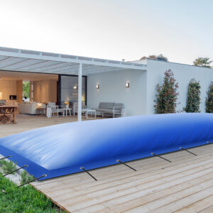 Das Äußere eines modernen Hauses verfügt über eine Holzterrasse mit rechteckigen aufblasbaren Poolplanen. Terrassenmöbel und Essbereich befinden sich unter einer Pergola, umgeben von üppigem Grün und vor der Kulisse eines klaren Himmels.