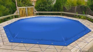 Eine blaue achteckige Poolplane deckt den Aufstellpool auf einem Holzdeck ab. Mit Kordeln und Ösen fest befestigt, steht sie zwischen Bäumen und einem Haus im Hintergrund.