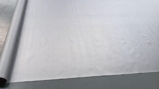 Eine große Rolle hellgrauer Stoff ähnlich dem LKW PVC Planen Reste, teilweise abgerollt mit einer weichen Textur, die subtil Licht einfängt und anmutig geschwungene Kanten hat.