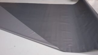 Eine Bahn aus glattem, dunkelgrauem Stoff erinnert an LKW PVC Planen Reste, ausgerollt auf hellgrauem Untergrund. Das leicht glänzende Material ist an einer Ecke partiell gefaltet.