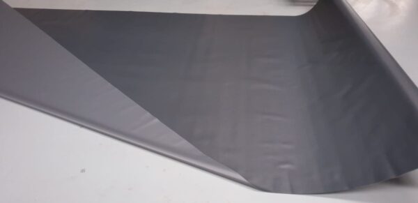 Eine Bahn aus glattem, dunkelgrauem Stoff erinnert an LKW PVC Planen Reste, ausgerollt auf hellgrauem Untergrund. Das leicht glänzende Material ist an einer Ecke partiell gefaltet.