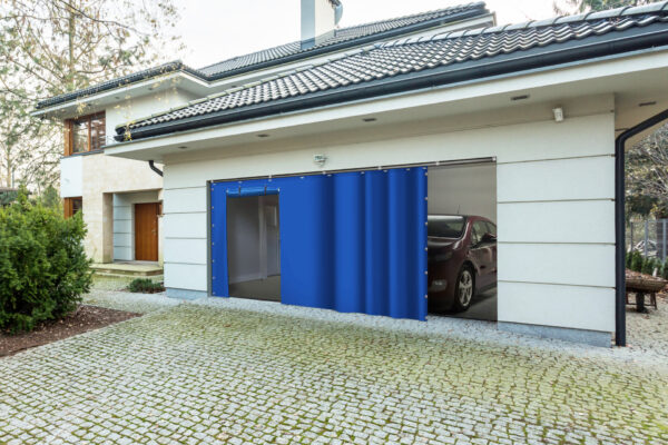 Ein modernes Haus mit geschlossener Holztür und teilweise geöffneter blauer Schiebetür zur Garage, hinter der ein geparktes Auto zu sehen ist. Die Garage hat eine gepflasterte Auffahrt, die von Grün umgeben ist.
