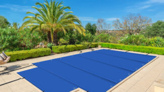Eine rechteckige Poolplane + Treppe (Stangenabdeckung) ist auf einem Pool in einem sonnigen Hinterhof mit gefliester Terrasse befestigt, umgeben von gut geschnittenen Hecken, üppigen Pflanzen und einer großen Palme unter einem klaren blauen Himmel.