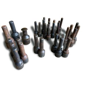 Eine Auswahl an Einschlagstempeln (Ösenwerkzeug) -Gebraucht-, bestehend aus verrosteten und dunklen Metallzylindern mit Griffen, die ordentlich in Reihen auf einem weißen Hintergrund angeordnet sind und sowohl große als auch kleine Werkzeuge zeigen.